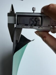 Digital caliper measuring the black conductive bottom layer of a 2 mm ESD bench mat at 1.55 mm, measured at the cut cross-section