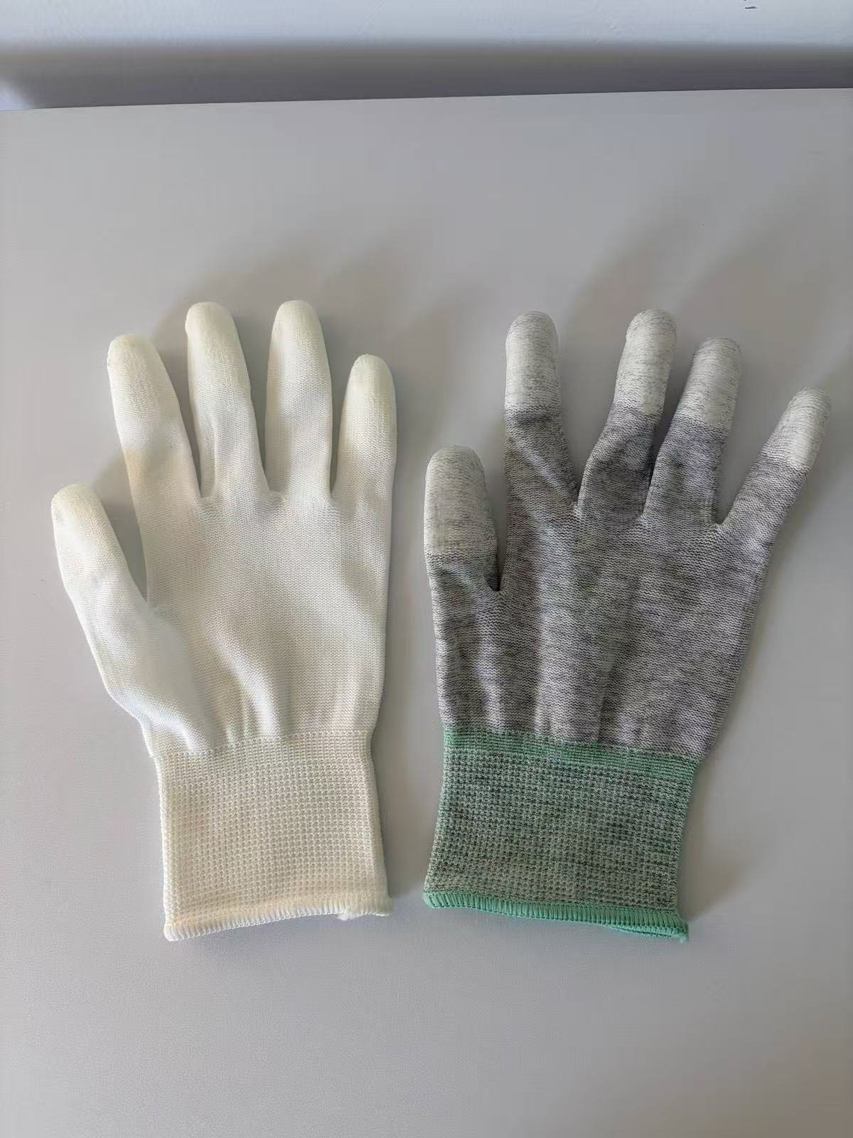 Carbon fibre ESD glove with grey knit and green cuff next to a plain white knitted glove, both with PU fingertip coating